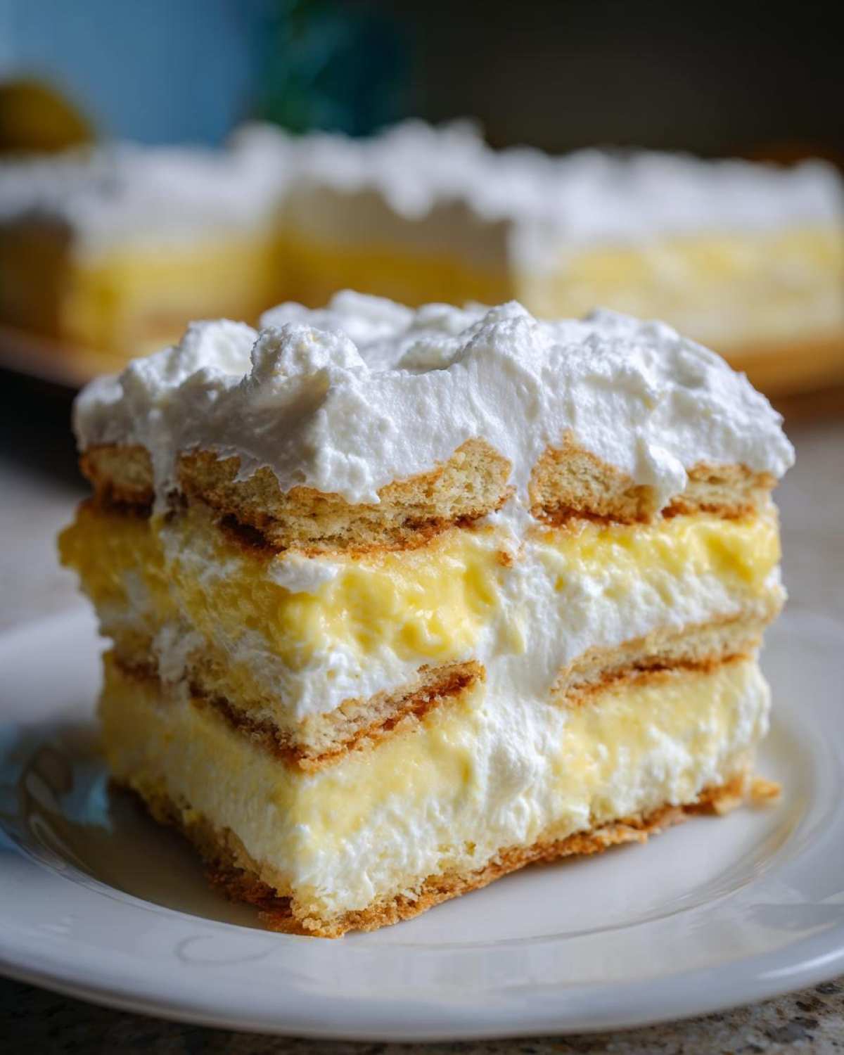 A close-up slice of No-Bake Lemon Icebox Cake showing layers of graham crackers, lemon filling, and whipped topping.