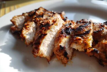 Close-up of sliced, grilled Copycat Chipotle Chicken showing char marks and juicy interior on a white plate.