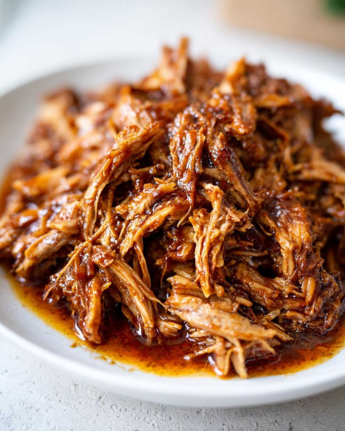 A close-up view of tender, shredded Slow Cooker Honey Garlic Pulled Pork coated in a rich, glossy sauce on a white plate.