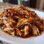 Close-up of tender, shredded Slow Cooker Honey Garlic Pulled Pork coated in a rich, glossy sauce on a white plate.