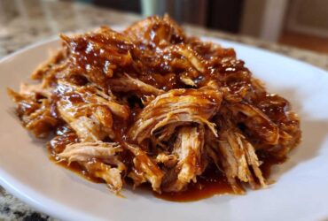 Close-up of tender, shredded Slow Cooker Honey Garlic Pulled Pork coated in a rich, glossy sauce on a white plate.