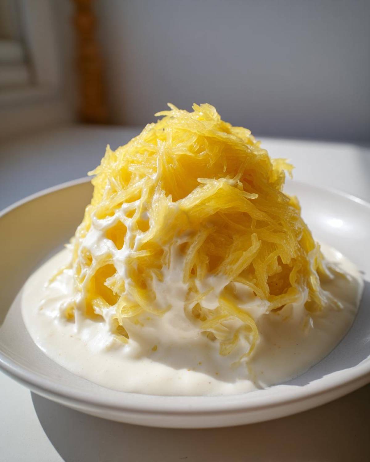 A mound of bright yellow spaghetti squash strands covered in rich, white Alfredo sauce, served in a white bowl.