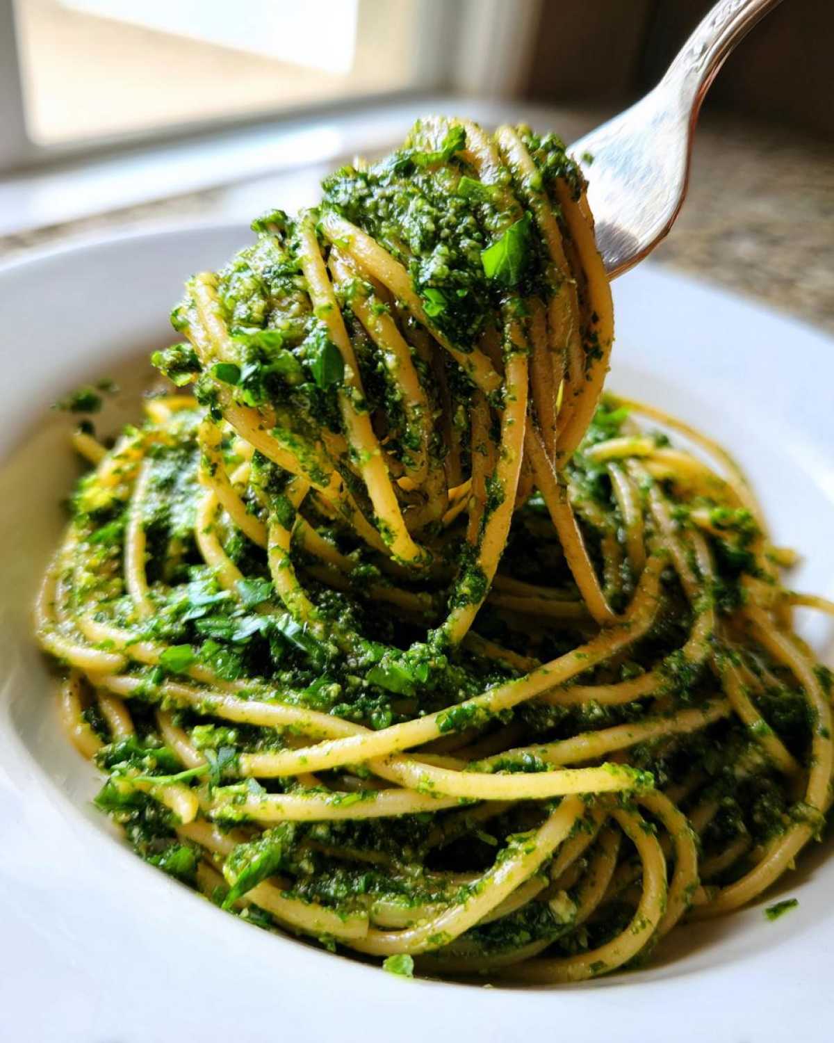 A fork lifting spaghetti coated generously in bright green Vegan Basil Pesto from a white bowl.