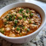 Close-up of a white bowl filled with rich, orange-red Spicy Turkey White Bean Chili, topped generously with chopped green onions.