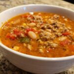 Close-up of a white bowl filled with rich, orange broth containing ground turkey, white beans, and diced tomatoes from the Spicy Turkey White Bean Chili.