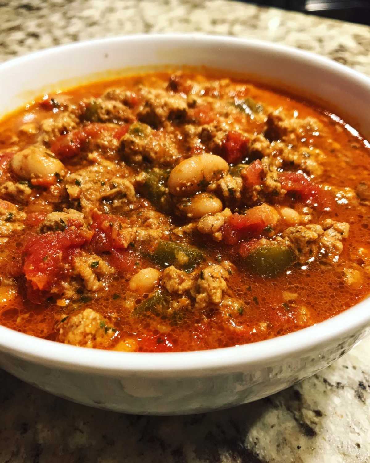Close-up of a white bowl filled with rich, red Spicy Turkey White Bean Chili featuring ground turkey, white beans, and tomatoes.