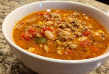 Close-up of a white bowl filled with rich, orange broth containing ground turkey, white beans, and diced tomatoes from the Spicy Turkey White Bean Chili.