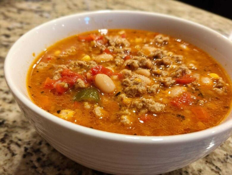 Close-up of a white bowl filled with rich, orange broth containing ground turkey, white beans, and diced tomatoes from the Spicy Turkey White Bean Chili.