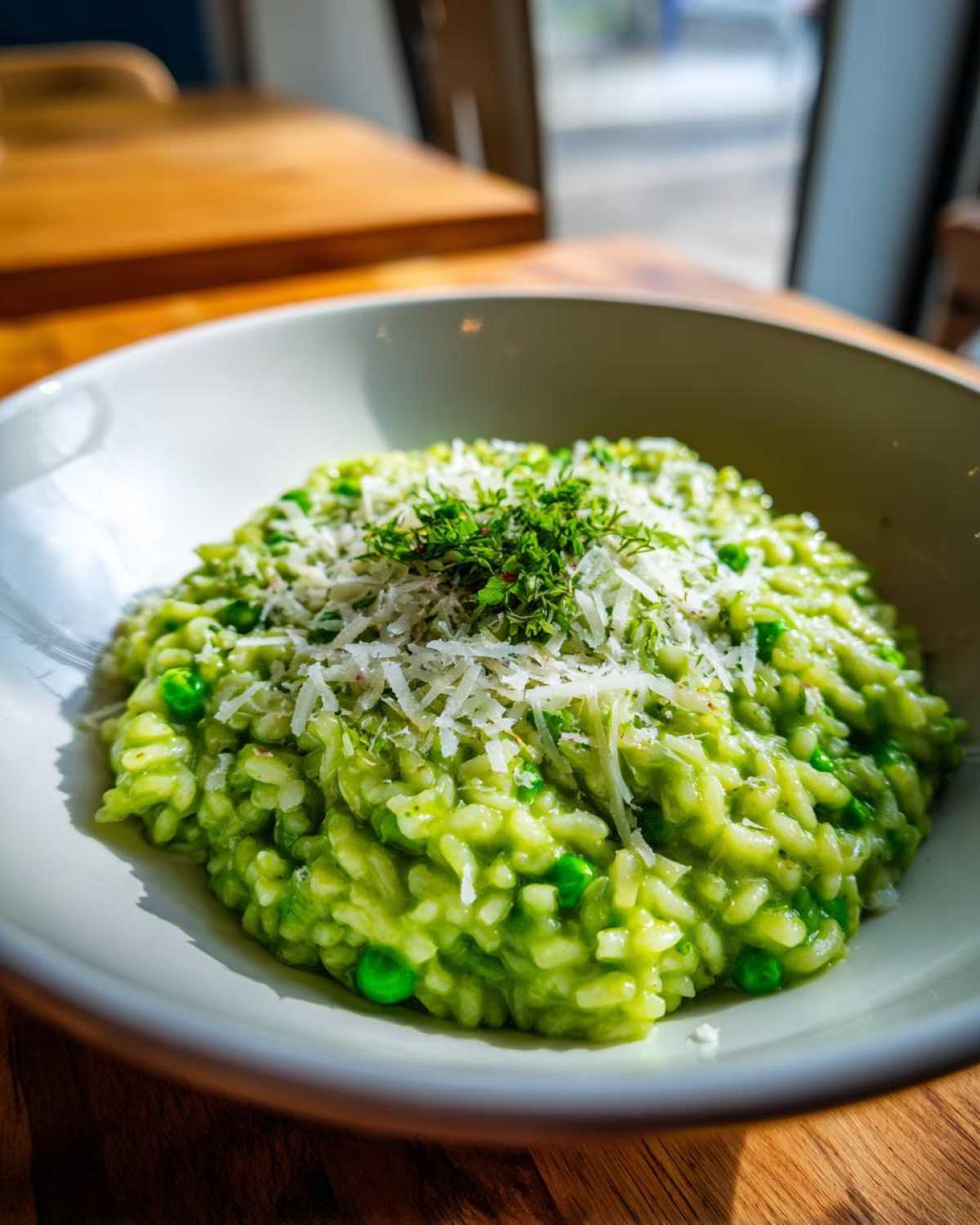 A close-up of vibrant green Spring Pea and Mint Risotto topped with grated Parmesan cheese and fresh herbs.