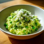 A close-up of creamy Spring Pea and Mint Risotto, topped generously with grated cheese and fresh herbs.