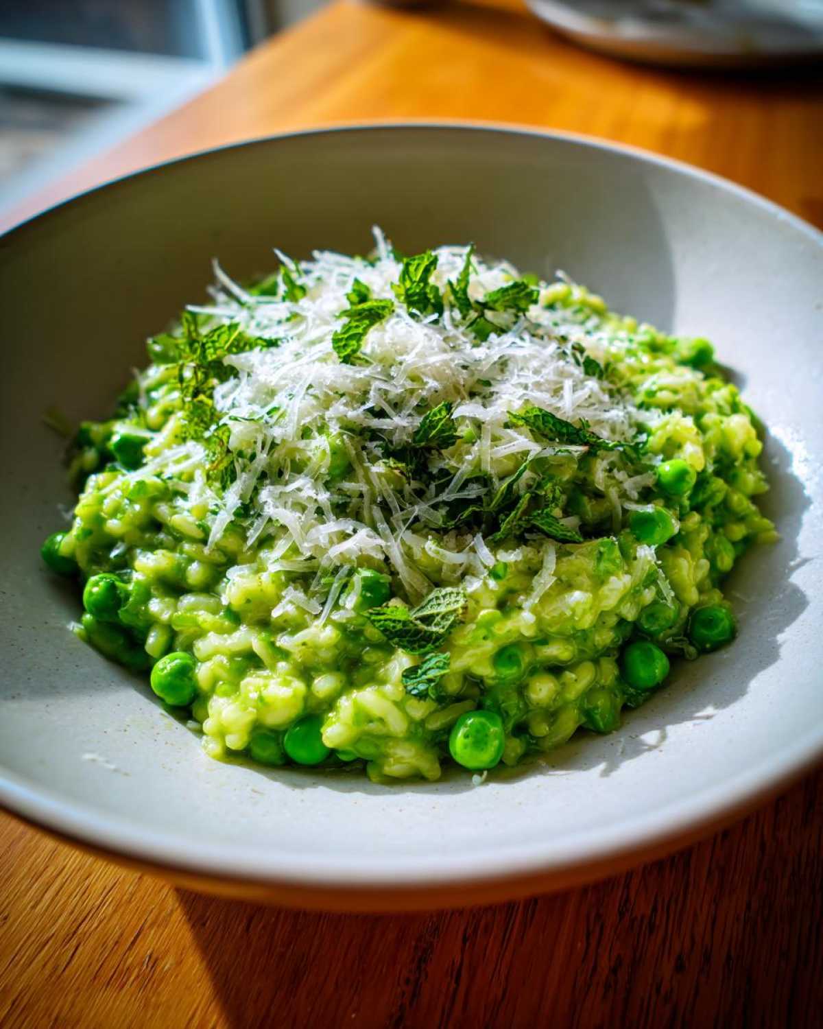 A close-up of creamy Spring Pea and Mint Risotto topped with shredded Parmesan cheese and fresh mint.