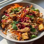 Close-up of a vibrant Spring Roll Bowl with Peanut Sauce, featuring rice noodles, crispy tofu, shredded carrots, cabbage, and fresh mint.