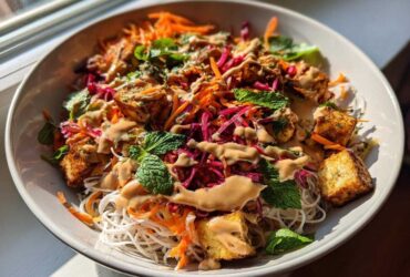 Close-up of a vibrant Spring Roll Bowl with Peanut Sauce, featuring rice noodles, crispy tofu, shredded carrots, cabbage, and fresh mint.