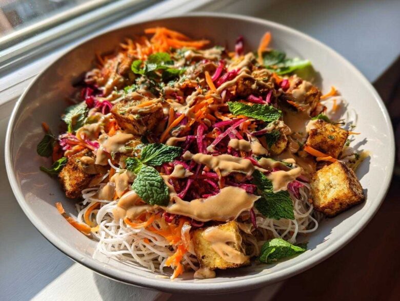 Close-up of a vibrant Spring Roll Bowl with Peanut Sauce, featuring rice noodles, crispy tofu, shredded carrots, cabbage, and fresh mint.