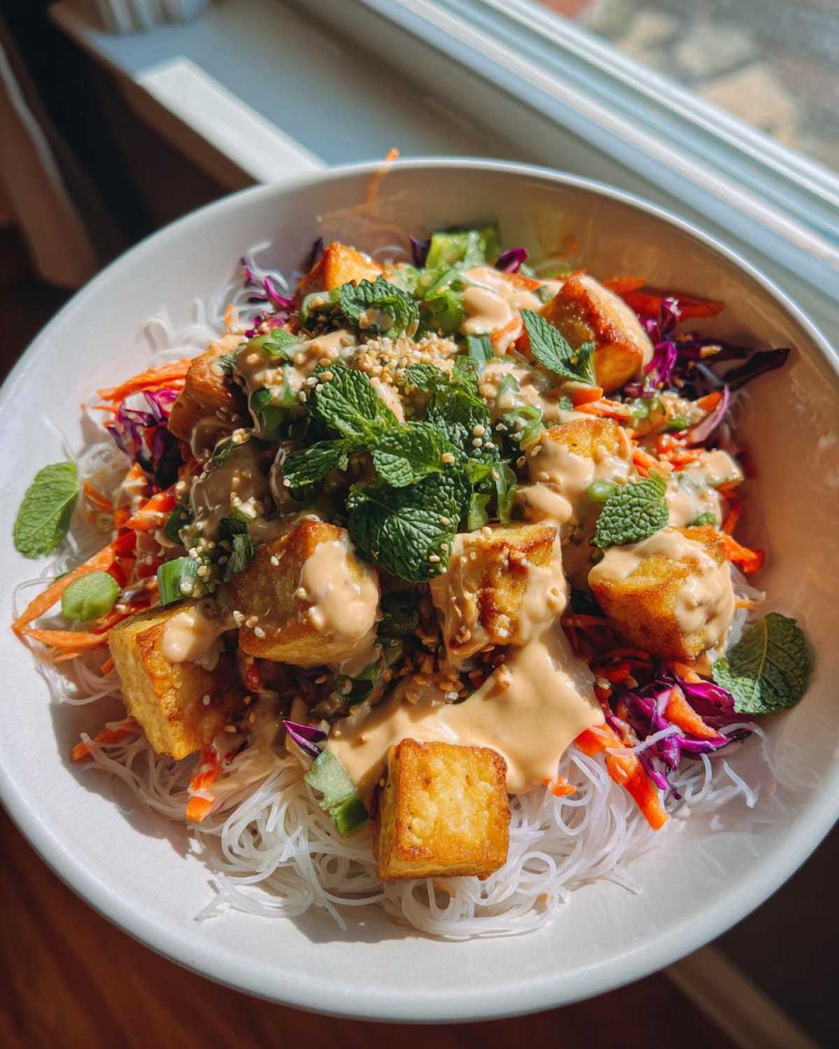 Close-up of a vibrant Spring Roll Bowl with Peanut Sauce, featuring crispy tofu, rice noodles, shredded carrots, red cabbage, and fresh mint.