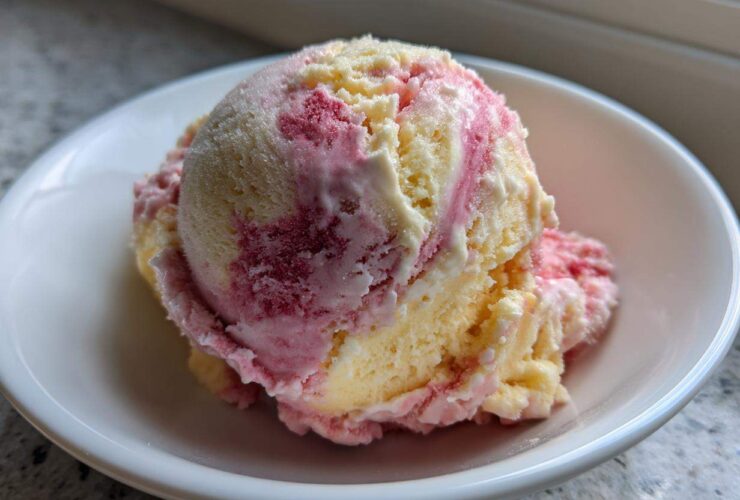 A close-up of two scoops of swirled Strawberry Banana Ice Cream, featuring yellow banana and pink strawberry swirls, served in a white bowl.