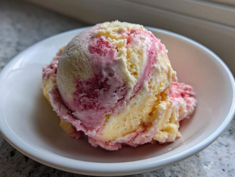 A close-up of two scoops of swirled Strawberry Banana Ice Cream, featuring yellow banana and pink strawberry swirls, served in a white bowl.