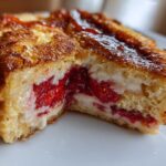 Close-up view of Strawberry Cream Cheese Stuffed French Toast, showing the golden-brown exterior and creamy filling with bright red strawberries.