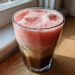 Close-up of a glass filled with layered Strawberry Cream Cold Brew, showing dark coffee below and pink foam on top.