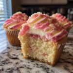 A close-up of a Strawberry Crunch Cupcakes with a bite taken out, revealing the moist cake and creamy filling.