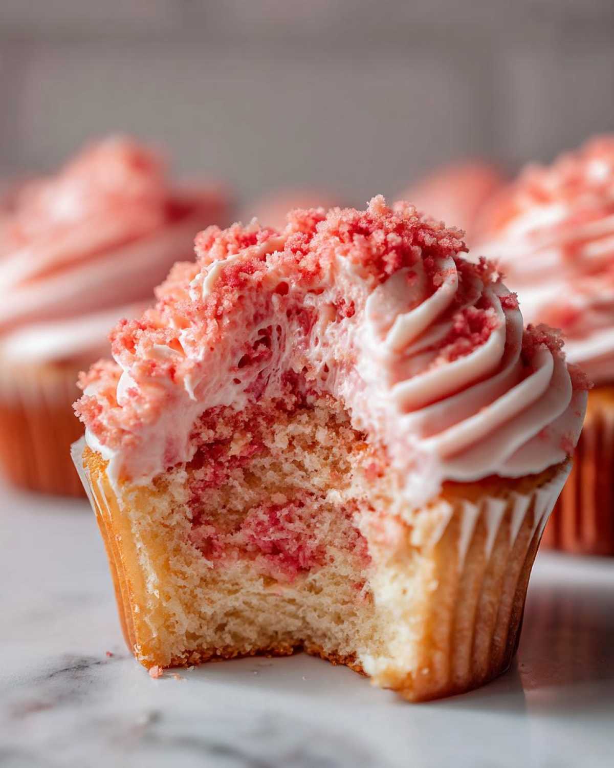 A close-up view of a Strawberry Crunch Cupcakes with a bite taken out, showing the moist cake and pink frosting topped with crunch.