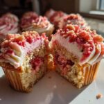A Strawberry Crunch Cupcakes cut in half showing the moist cake, pink filling, white frosting, and strawberry crunch topping.