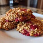 A stack of three freshly baked Strawberry Oatmeal Breakfast Cookies with visible oats and bright red strawberry filling on a white plate.