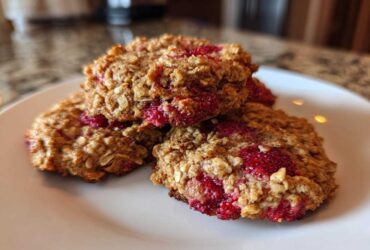 A stack of three freshly baked Strawberry Oatmeal Breakfast Cookies with visible oats and bright red strawberry filling on a white plate.