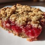 Close-up of a juicy slice of Strawberry Rhubarb Crisp showing the bright red fruit filling and crumbly topping.