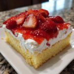 A close-up of a square slice of Strawberry Shortcake Sheet Cake topped with whipped cream and fresh strawberries in glaze.
