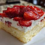Close-up of a moist slice of Strawberry Shortcake Sheet Cake featuring a light sponge base, whipped cream, and glossy glazed strawberries.