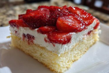 Close-up of a moist slice of Strawberry Shortcake Sheet Cake featuring a light sponge base, whipped cream, and glossy glazed strawberries.