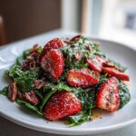 A vibrant close-up of Strawberry Spinach Salad tossed in dressing, featuring bright red strawberries and pecans on a white plate.