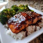 Close-up of a Teriyaki Salmon Rice Bowls serving with glossy teriyaki glaze and sesame seeds over white rice and broccoli.