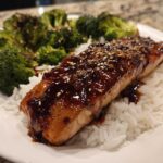 A close-up of a Teriyaki Salmon Rice Bowls serving featuring a glazed salmon fillet over white rice and steamed broccoli.