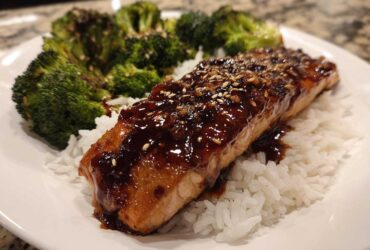 A close-up of a Teriyaki Salmon Rice Bowls serving featuring a glazed salmon fillet over white rice and steamed broccoli.