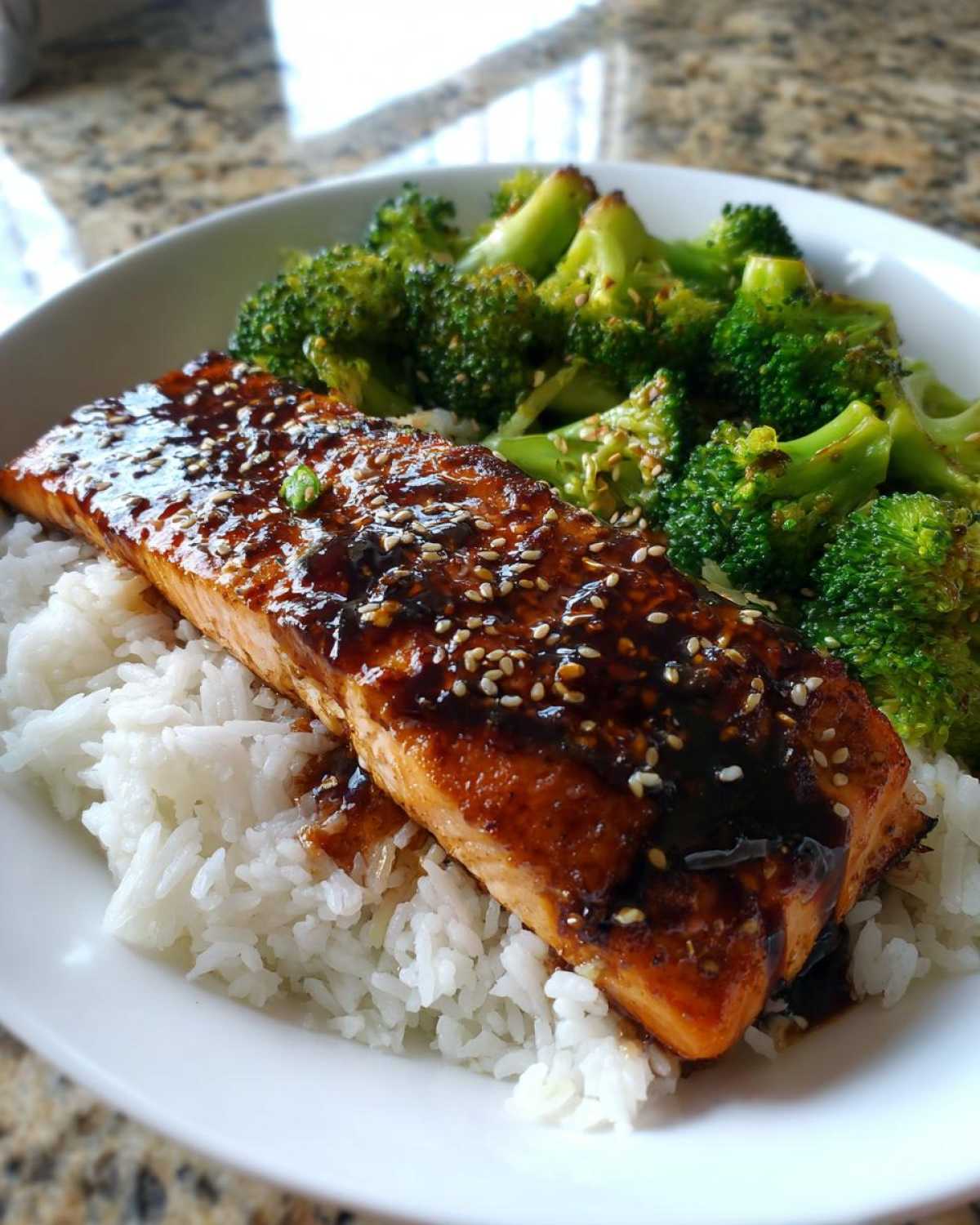 A close-up of a Teriyaki Salmon Rice Bowls serving featuring glazed salmon over white rice with steamed broccoli.