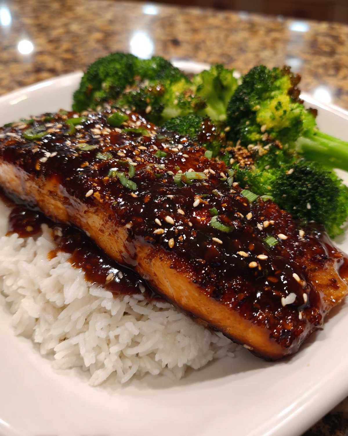 A close-up of a Teriyaki Salmon Rice Bowls serving featuring glazed salmon over white rice with steamed broccoli.