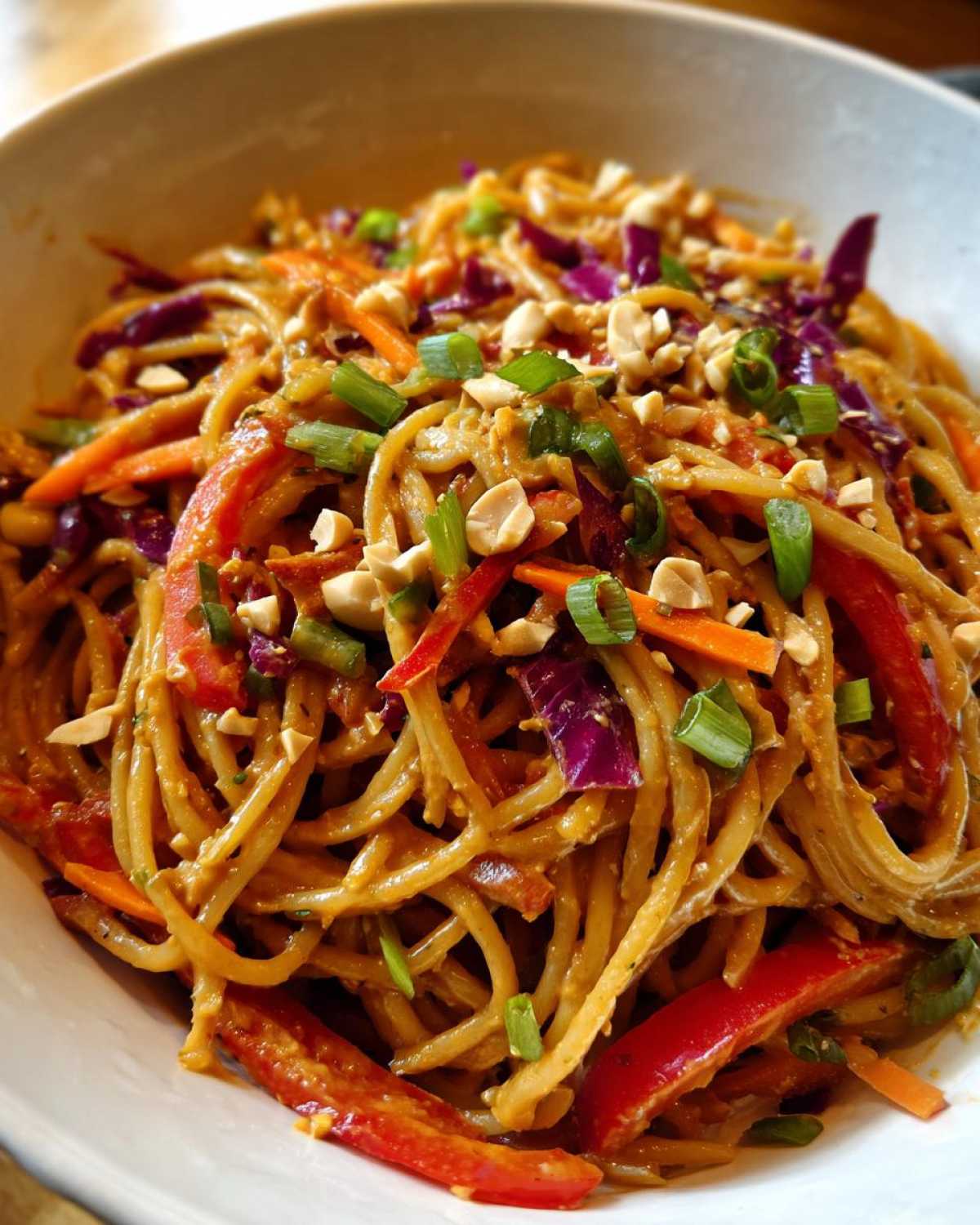 Close-up of a bowl filled with creamy Thai Peanut Noodles with Crunchy Veggies, topped with peanuts and scallions.