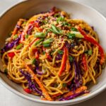 A close-up bowl of Thai Peanut Noodles with Crunchy Veggies, topped with peanuts and green onions.