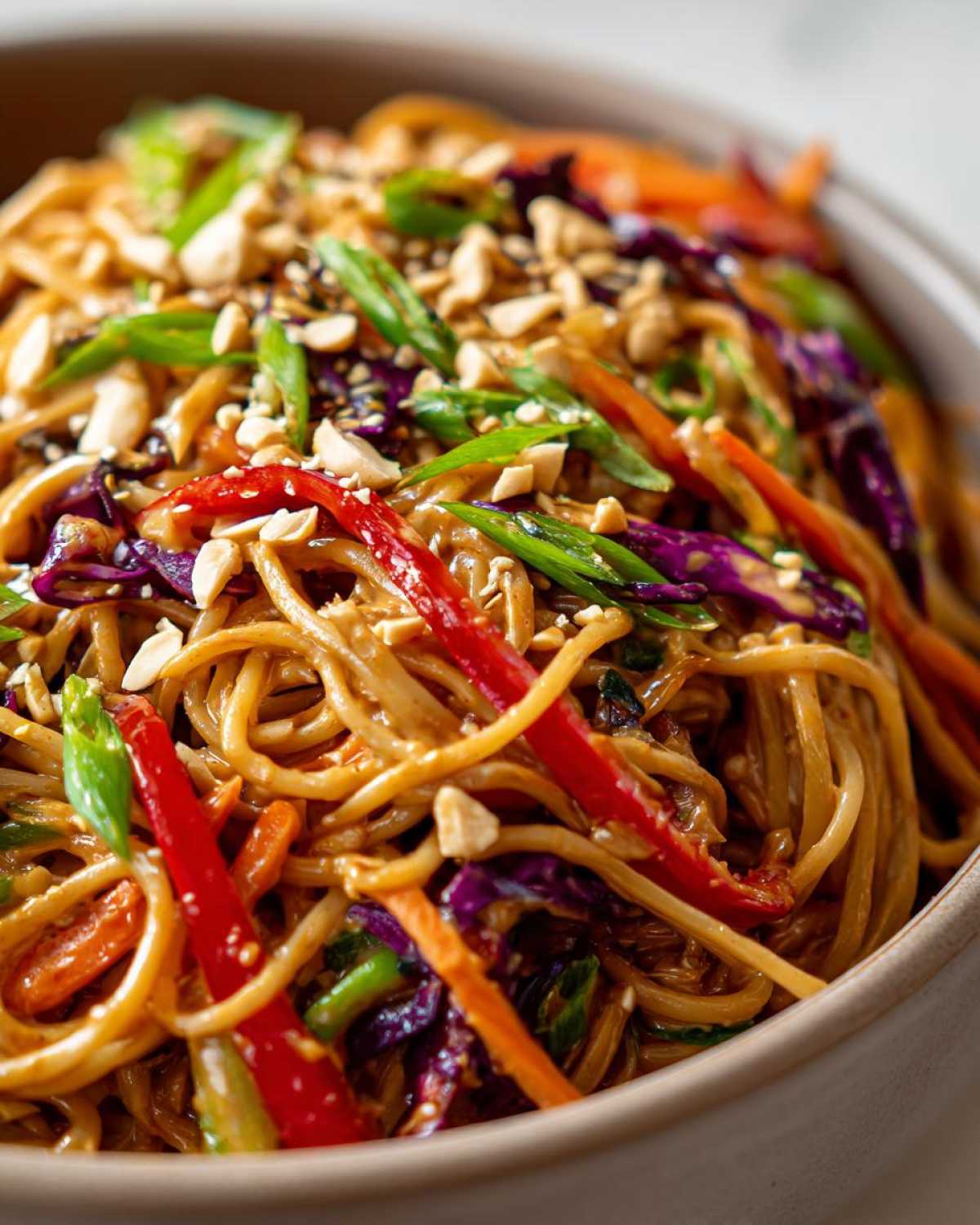Close-up of a bowl of Thai Peanut Noodles with Crunchy Veggies, topped with chopped peanuts and scallions.