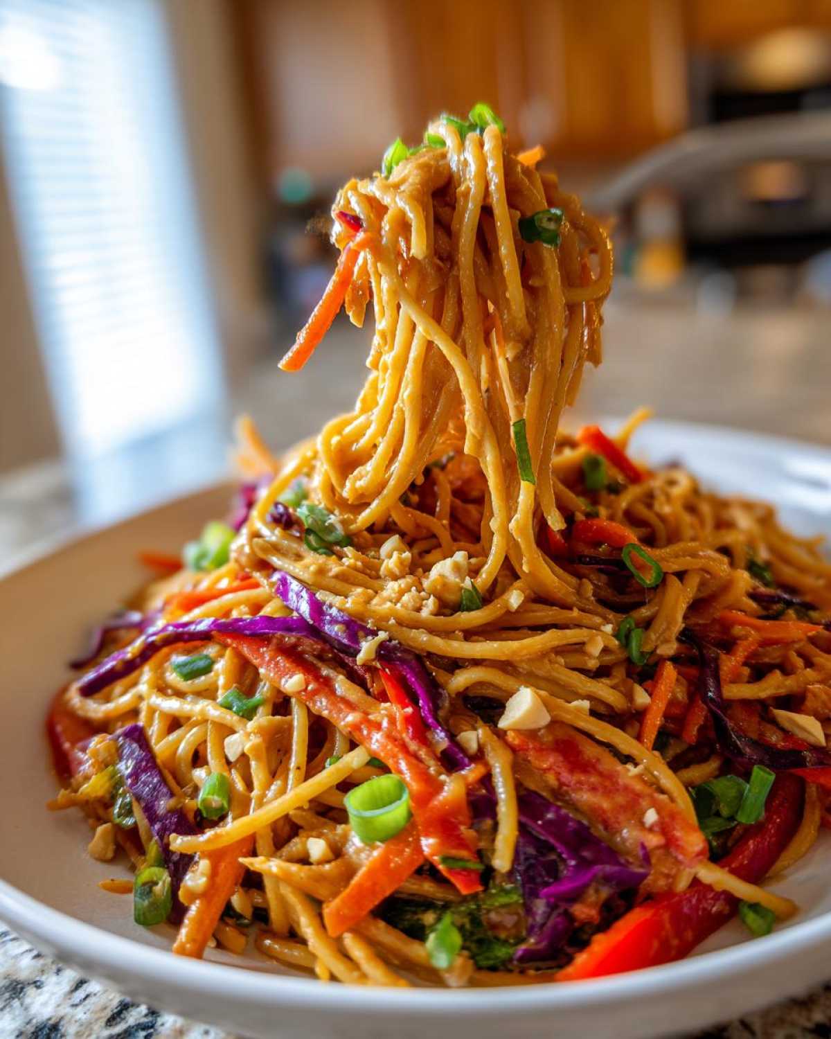 A fork lifts a large portion of creamy Thai Peanut Noodles with Crunchy Veggies, showing julienned carrots and purple cabbage.