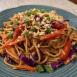 A close-up serving of Thai Peanut Noodles with Crunchy Veggies, topped with crushed peanuts and green onions.