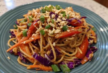 A close-up serving of Thai Peanut Noodles with Crunchy Veggies, topped with crushed peanuts and green onions.