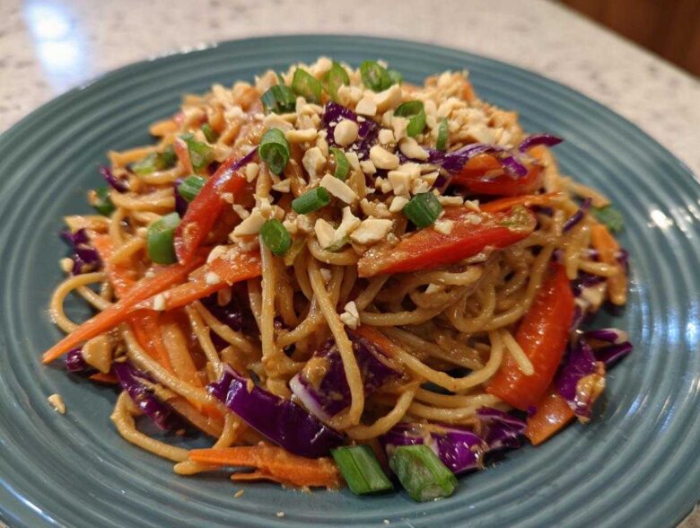 A close-up serving of Thai Peanut Noodles with Crunchy Veggies, topped with crushed peanuts and green onions.