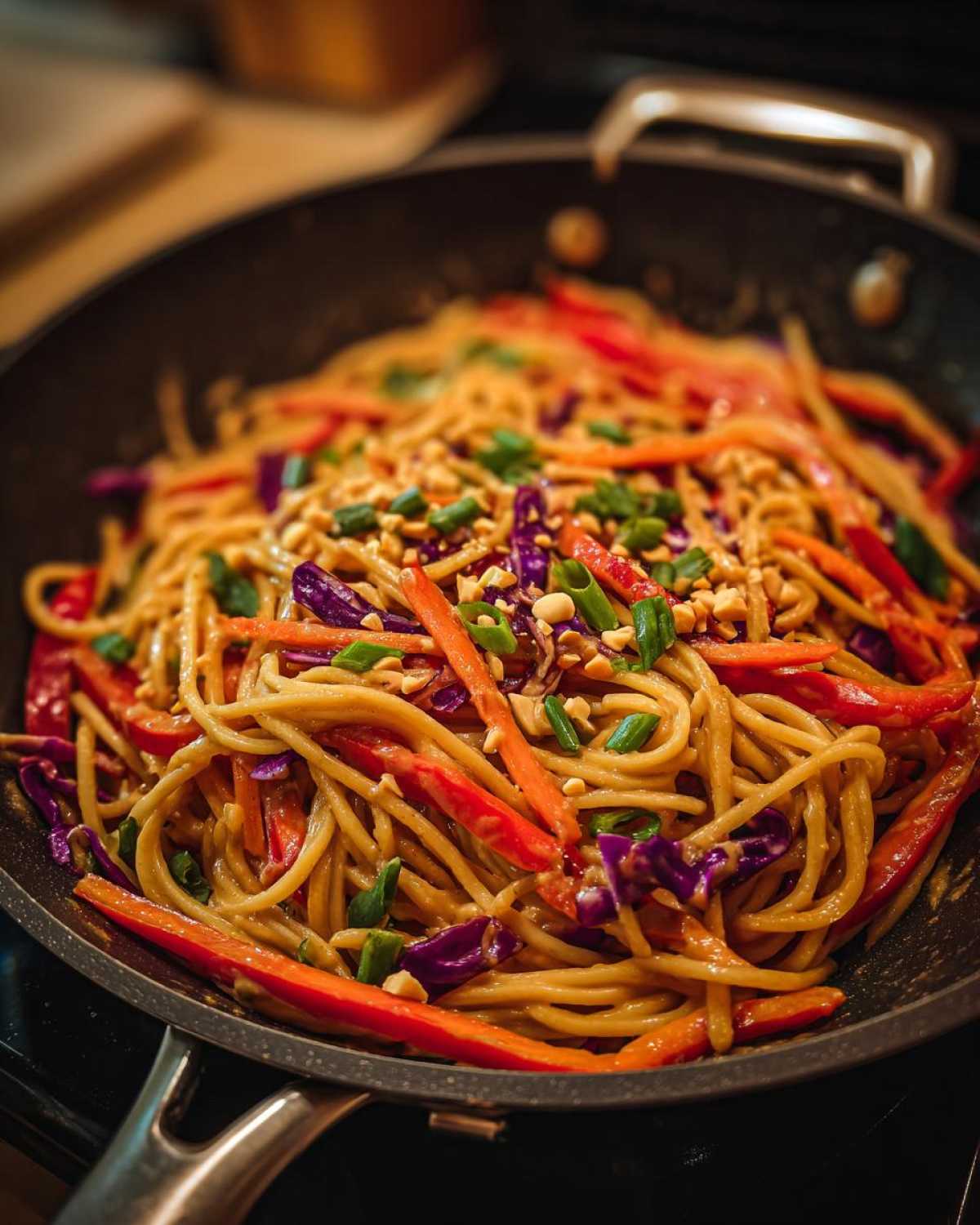 Close-up of Thai Peanut Noodles with Crunchy Veggies tossed in peanut sauce in a black skillet, topped with peanuts and scallions.