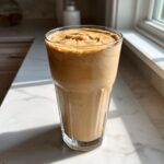 A thick, creamy Banana Peanut Butter Smoothie served in a tall glass on a sunny marble countertop.