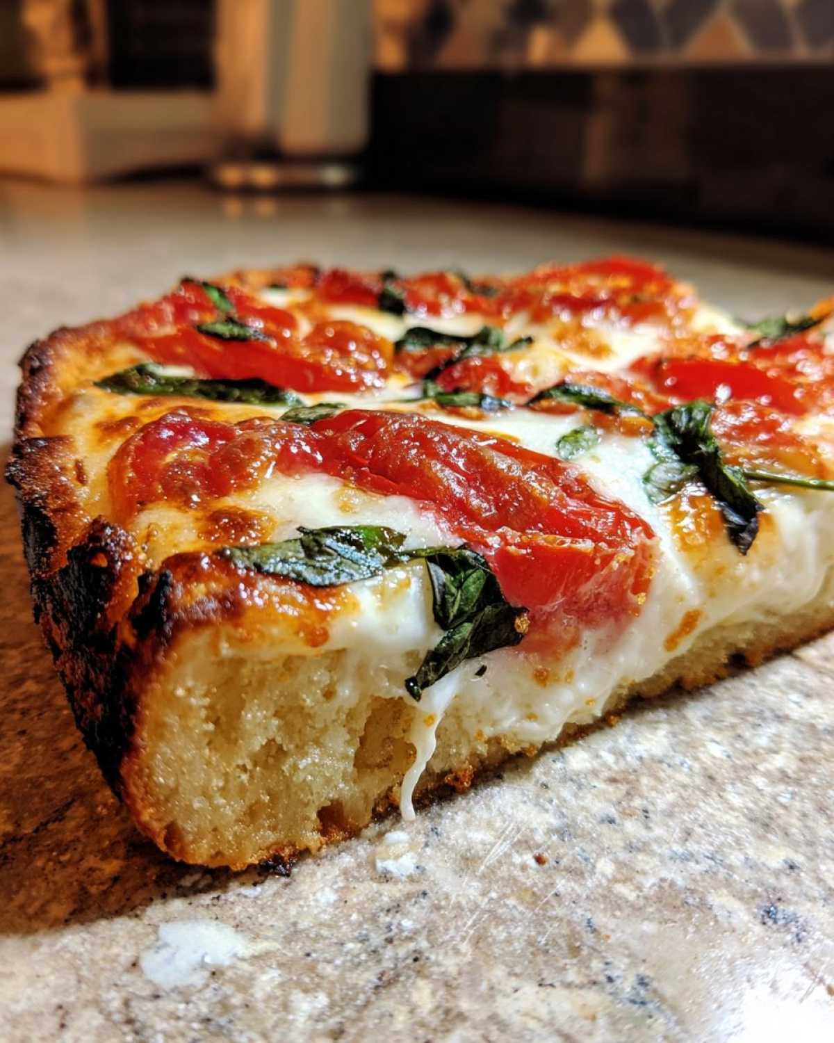 Close-up of a thick, square slice of Gluten-Free Margherita Pizza showing the airy crust, melted mozzarella, tomatoes, and basil.