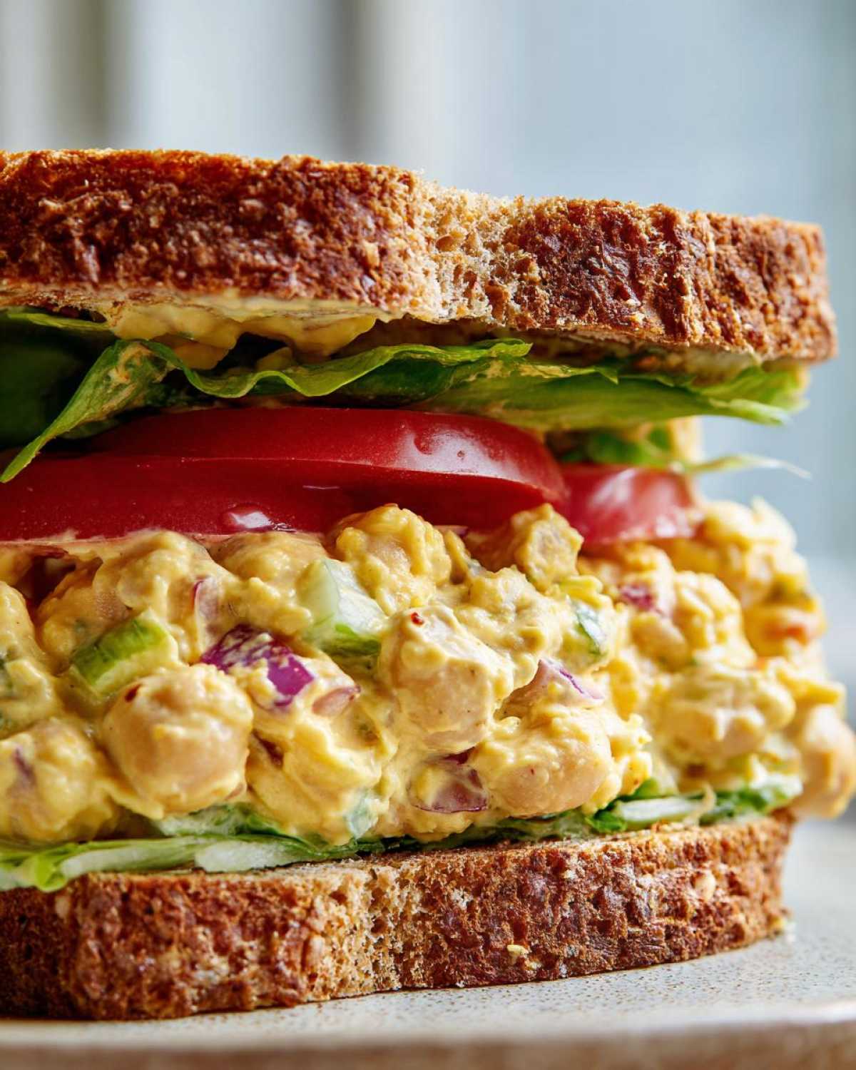 Close-up of a hearty Vegan Chickpea Salad Sandwich layered with creamy chickpea salad, tomato, and lettuce on whole wheat bread.