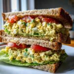 A tall, stacked Vegan Chickpea Salad Sandwich made with whole wheat bread, lettuce, tomato slices, and creamy chickpea filling.